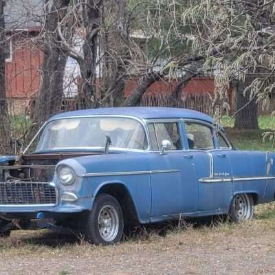 Old blue car parked next to a tire stack.