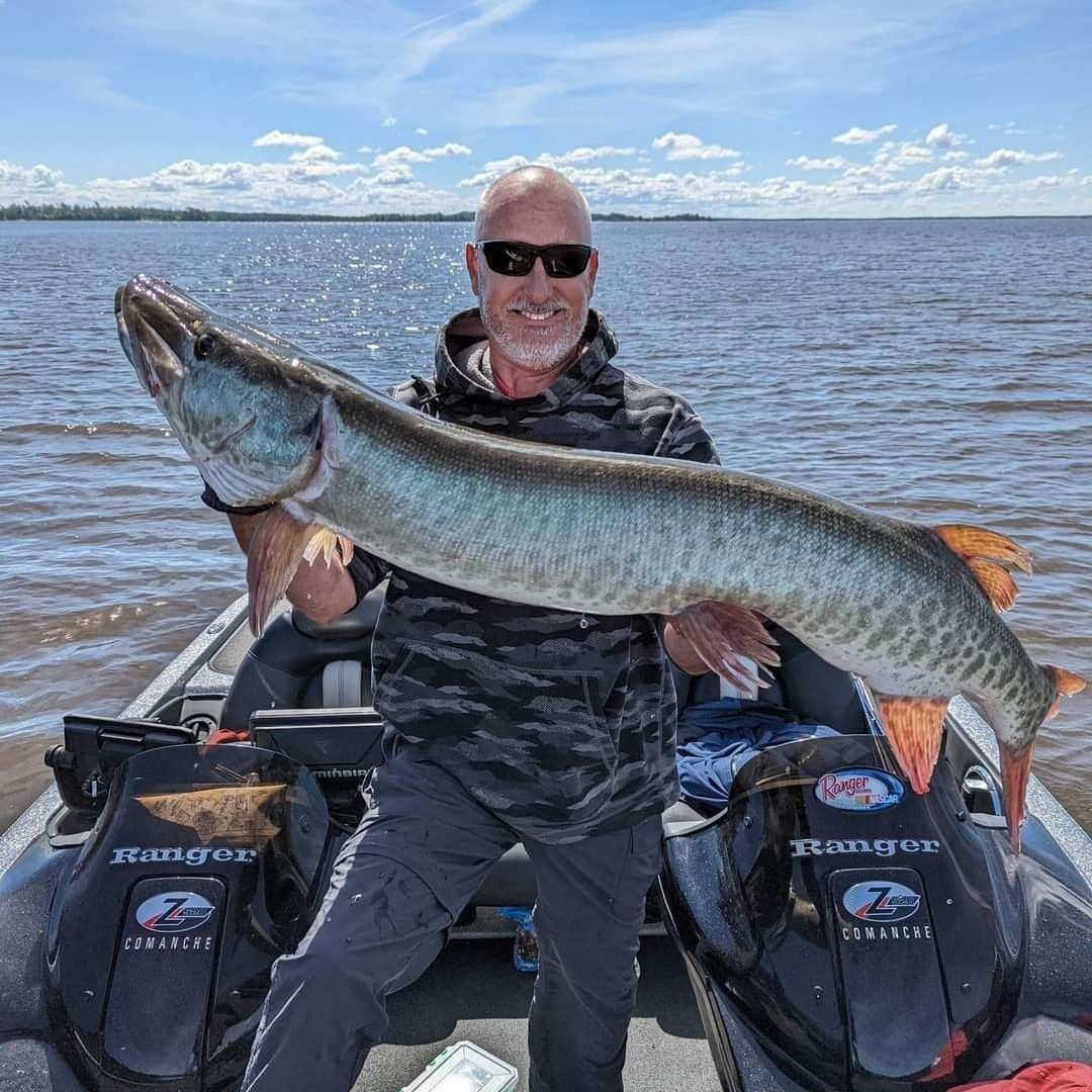 Man holding large fish on boat with lake.
