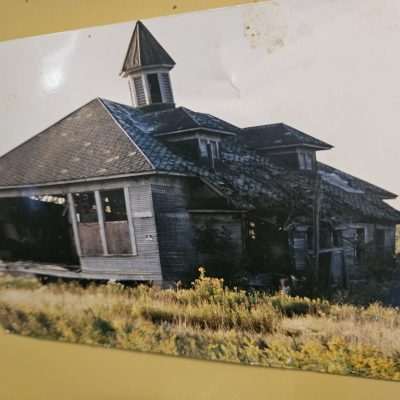 Abandoned house with broken roof and overgrown vegetation.