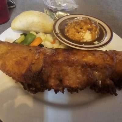 Fried fish with mashed potatoes, gravy, and vegetables on plate