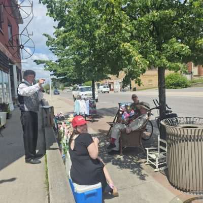 People enjoying a sidewalk sale in sunny weather.