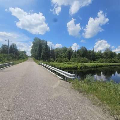 Scenic rural road bridge over river with cloudy sky.