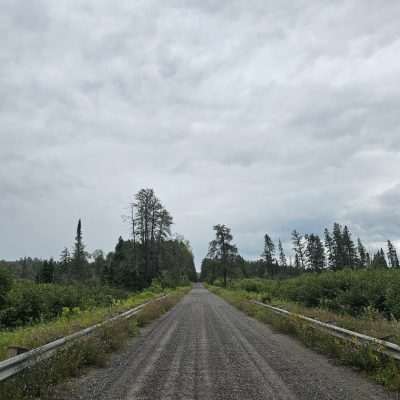 Gravel road through forest under cloudy sky on the Ottowa National Forest.