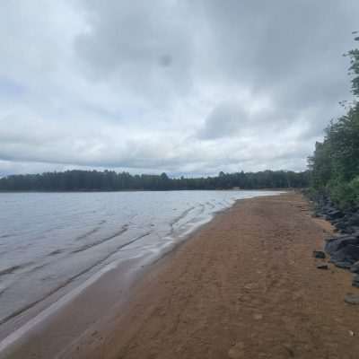 Sandy beach beside a calm lake and trees.