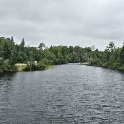 Forest-lined lake under cloudy sky.