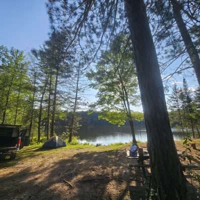 Campsite by a tranquil lakeside surrounded by trees.