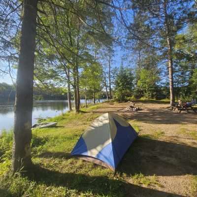 Tent in a forested lakeside campsite.