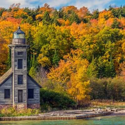 Lighthouse surrounded by vibrant autumn foliage by water.